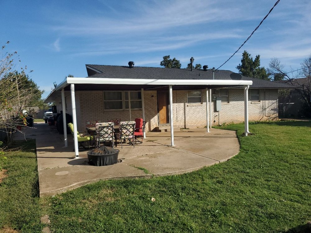 An image showing a brick house with a covered porch and chairs outside on a grassy lawn.